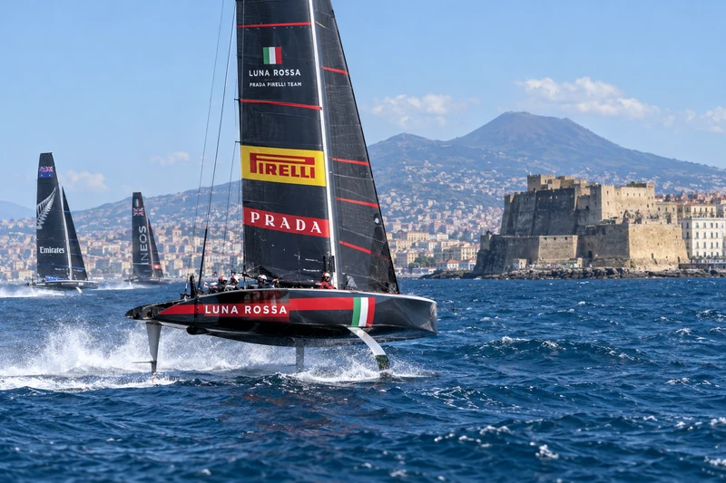 L’AC40 di Luna Rossa in foiling nel Golfo di Napoli con Castel dell’Ovo sullo sfondo; scena editoriale IA non documentaria.
