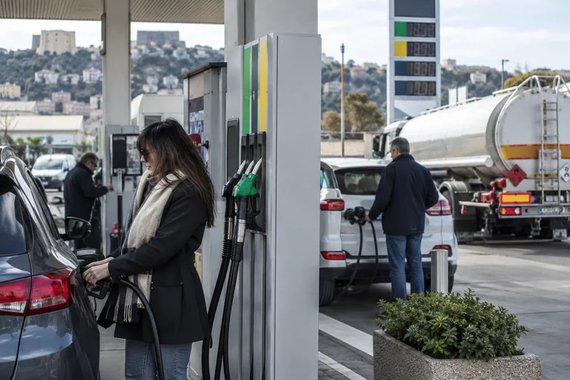 Scena editoriale contestuale ordinaria generata con IA di automobilisti in una stazione di servizio italiana