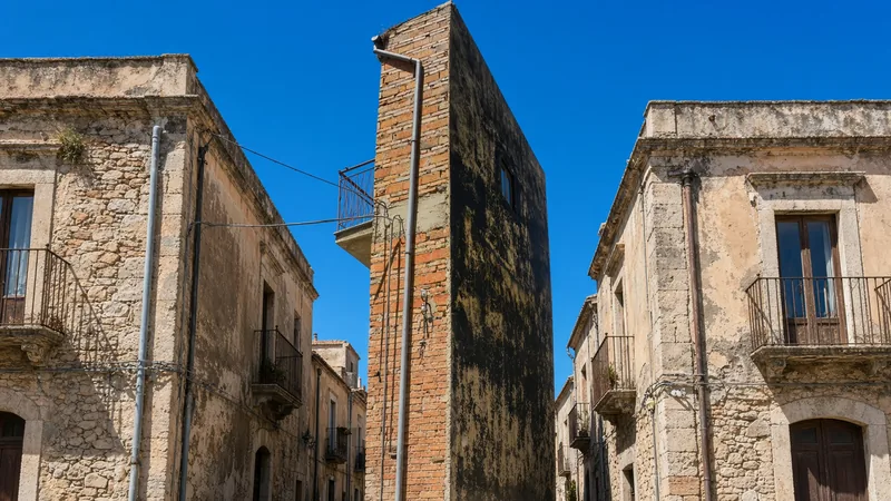 Casa del dispetto strettissima in mattoni e intonaco nero tra case di un borgo siciliano; illustrazione editoriale IA non documentaria.