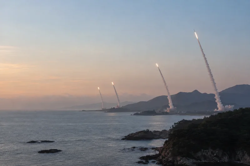 Scena editoriale contestuale ordinaria generata con IA di lanci missilistici lontani dalla costa di Wonsan verso il mare, senza persone visibili