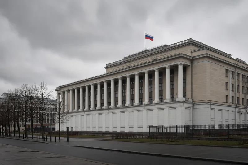 Illustrazione editoriale generata con IA: facciata della Duma di Stato a Mosca in una mattina nuvolosa, marciapiede quasi vuoto, senza scritte editoriali; non è una fotografia documentaria.