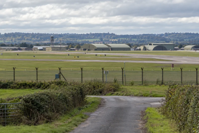Illustrazione IA di una pista e hangar della base RAF Fairford dietro una recinzione, senza persone o ordigni.
