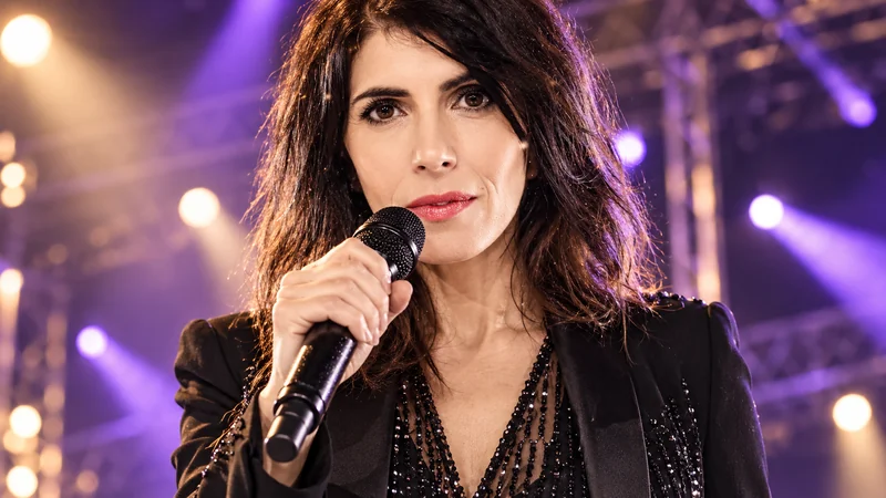 Somiglianza sintetica editoriale di Giorgia con microfono e luci da concerto; scena IA non documentaria.