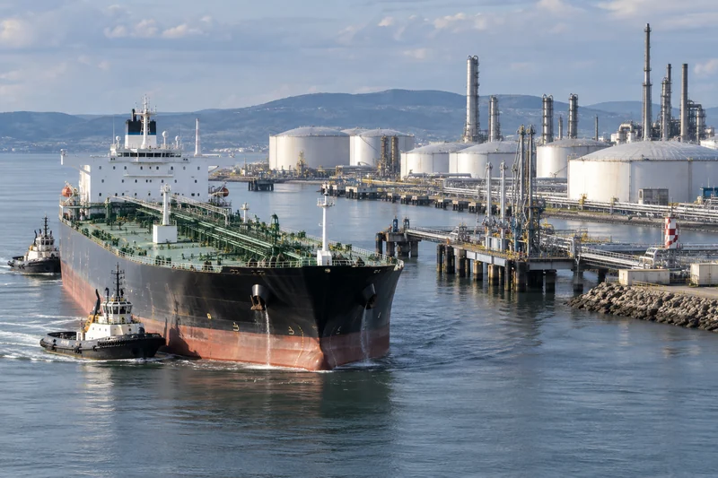 Illustrazione editoriale generata con IA di una petroliera in un porto energetico europeo con serbatoi e condotte; non è una fotografia documentaria.