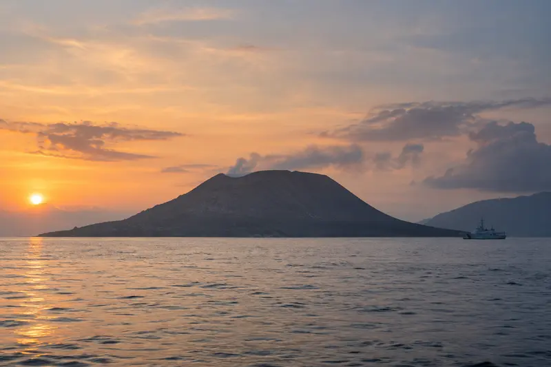 Paesaggio editoriale generato con IA dell'isola vulcanica Anak Krakatau nello Stretto della Sonda all'alba, con pennacchio di vapore; nessun disperso né relitto; non documentaria.
