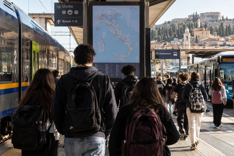 Illustrazione editoriale IA di studenti pendolari in un nodo ferroviario e autobus italiano; scena non documentaria.