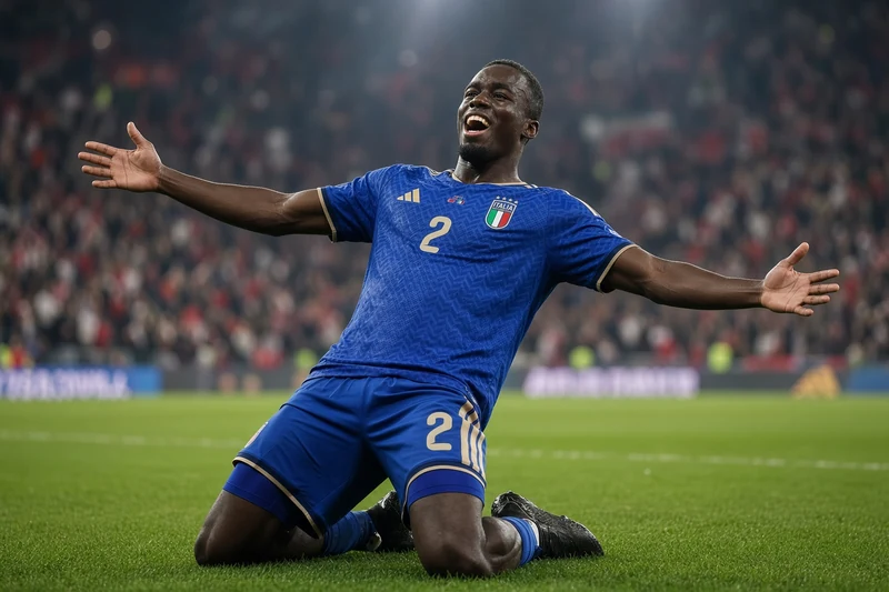 Michael Kayode in maglia azzurra numero 2 celebra in ginocchio il gol del debutto in Nazionale, braccia aperte sullo stadio.