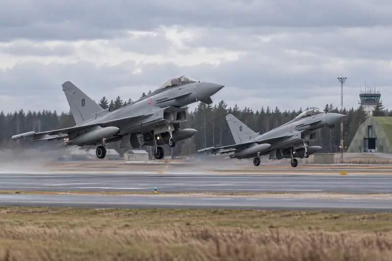 Scena editoriale contestuale generata con IA: due Eurofighter italiani in decollo da una base baltica; non documentaria.