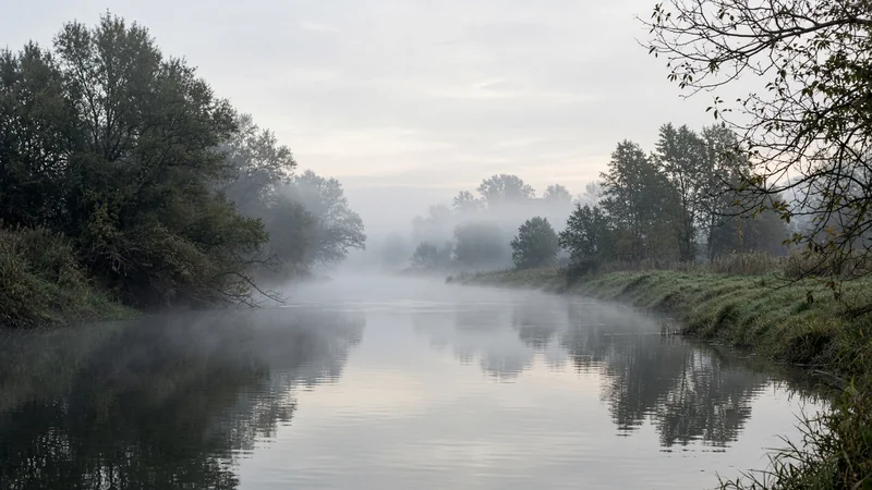 Fiume largo in campagna veneta al mattino, con una gru lontana sull'argine e nessuna persona
