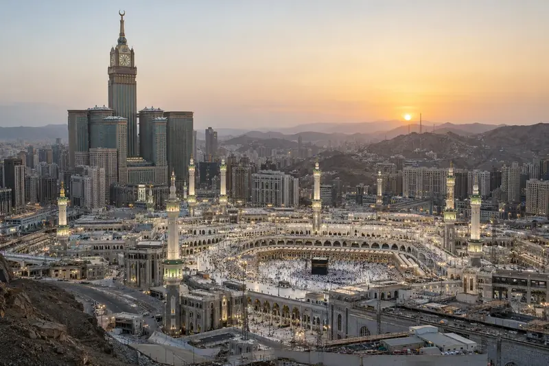 Illustrazione editoriale contestuale generata con IA: veduta realistica della Mecca all’alba, senza ricostruire l’intercettazione segnalata.