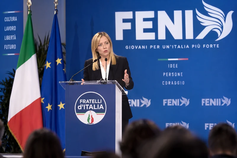 Illustrazione editoriale generata con IA: Giorgia Meloni parla sul palco di FENIX con bandiere italiana ed europea e loghi FENIX e Fratelli d’Italia visibili; non è una fotografia documentaria.