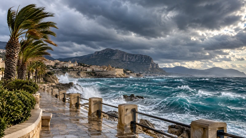 Costa dell’Italia meridionale con vento forte, palme piegate e mare molto mosso