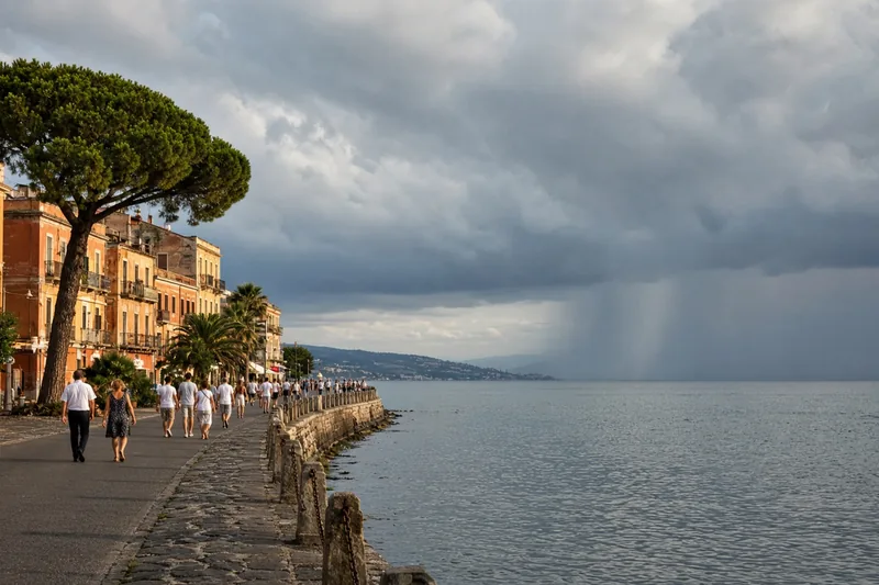 Illustrazione editoriale generata con IA: costa italiana a fine settembre con sole sulle facciate e nubi temporalesche sul mare, senza vittime né scritte; non è una fotografia documentaria.