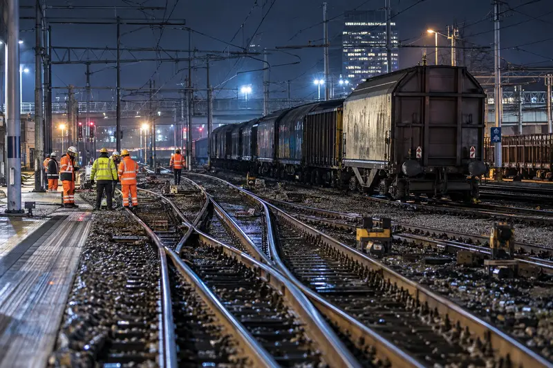 Illustrazione editoriale IA di un nodo ferroviario notturno con un treno merci fermo e tecnici sui binari; non è una fotografia dell'incidente di Milano Greco Pirelli.