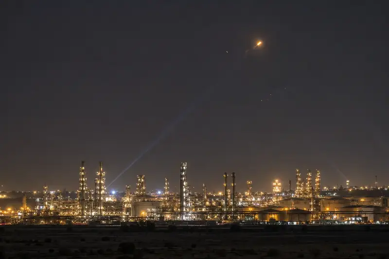 Raffineria saudita illuminata di notte mentre la difesa aerea intercetta un oggetto lontano