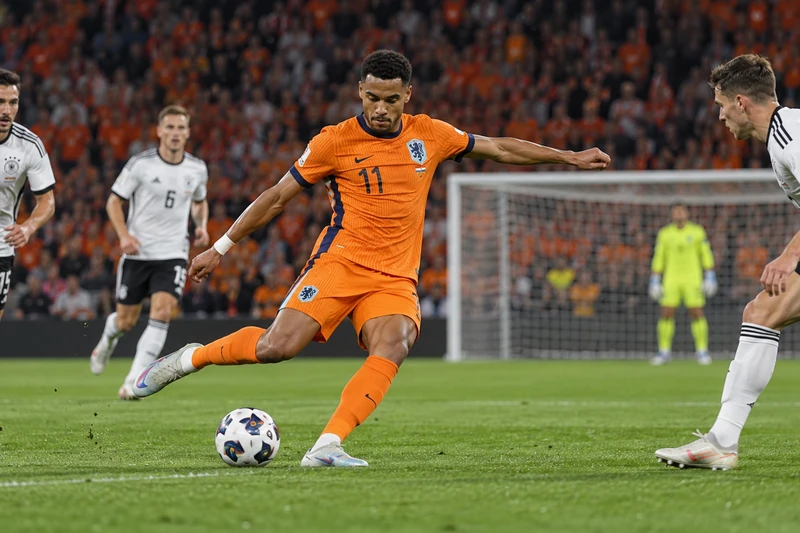 Foto d'archivio di Cody Gakpo, in maglia arancione dell'Olanda, che calcia verso la porta durante Olanda-Germania di Nations League, con i giocatori tedeschi in maglia bianca.