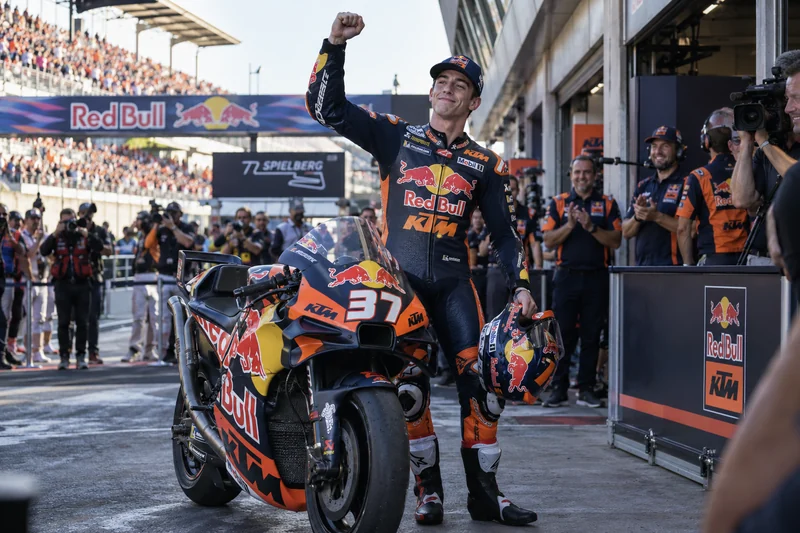 Illustrazione editoriale generata con IA: Pedro Acosta accanto alla KTM numero 37 nel paddock del Red Bull Ring, con le scritte e i loghi sportivi pertinenti visibili; non è una fotografia documentaria.