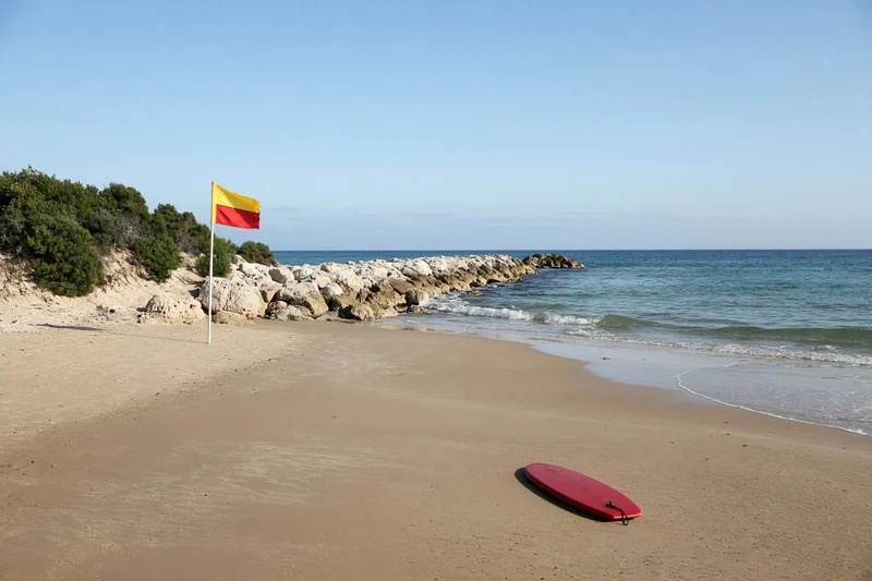 Illustrazione editoriale contestuale generata con IA: spiaggia vuota a nord di Perth, groyne di calcare e bandiera di chiusura, senza ricostruire l'attacco.