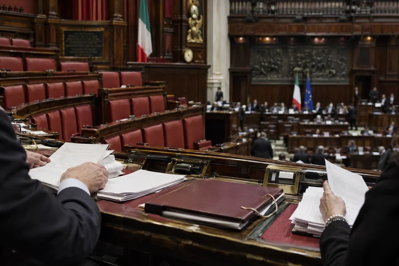 Scena editoriale contestuale generata con IA: documenti parlamentari nell’aula italiana durante l’iter della legge elettorale; non è una fotografia documentaria.