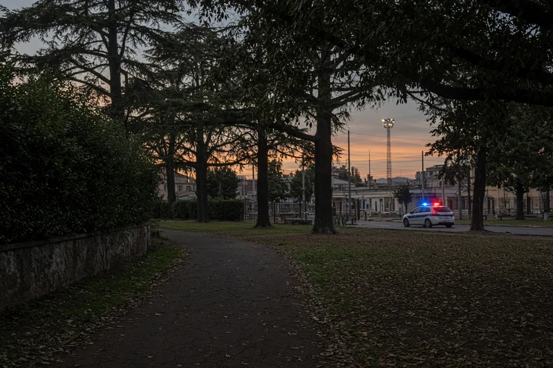 Illustrazione editoriale IA di un parco sobrio vicino a stazione a Roma al crepuscolo con auto di polizia lontana; non è una fotografia documentaria.