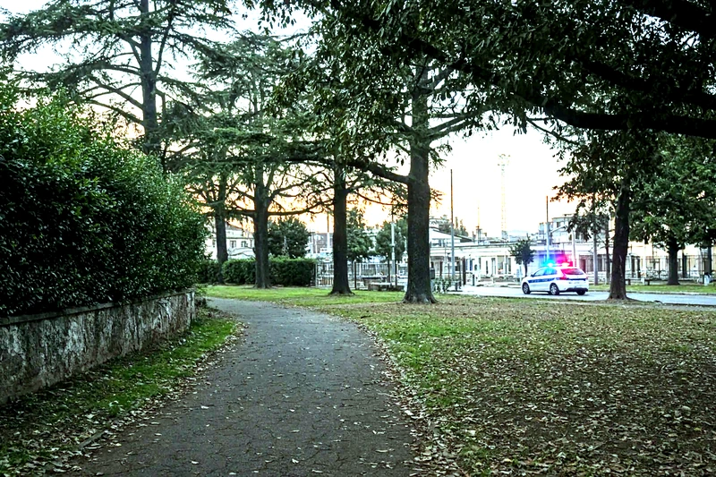 Illustrazione editoriale IA di un parco sobrio vicino a stazione a Roma al crepuscolo con auto di polizia lontana; non è una fotografia documentaria.