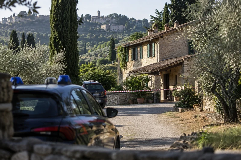 Foto d'archivio di auto dei Carabinieri davanti a un casale in pietra circondato da ulivi in campagna toscana, con nastro segnaletico all'ingresso.