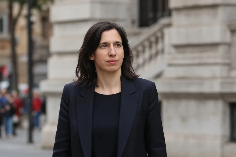 Scena editoriale contestuale generata con IA: Elly Schlein riconoscibile all’aperto a Roma; somiglianza sintetica, non una fotografia documentaria.