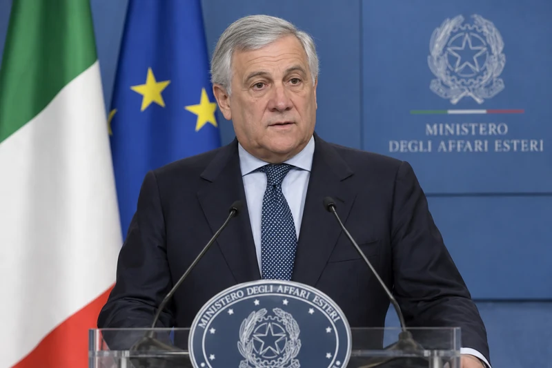 Ritratto editoriale neutrale generato con IA di Antonio Tajani al podio del Ministero degli Affari Esteri, con bandiere italiana ed europea; non è una fotografia documentaria.