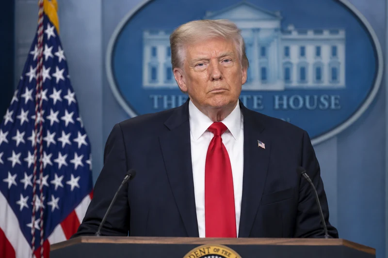 Ritratto editoriale neutrale generato con IA di Donald Trump al podio della Casa Bianca, con bandiera statunitense; non è una fotografia documentaria dell’intervista citata.
